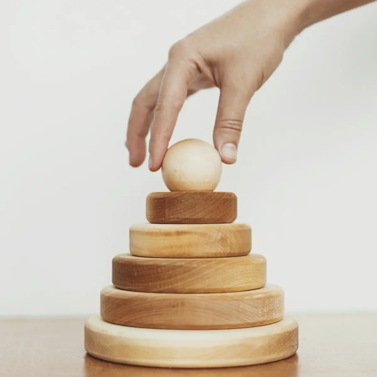 a hand stacking a wooden ball on four wooden discs